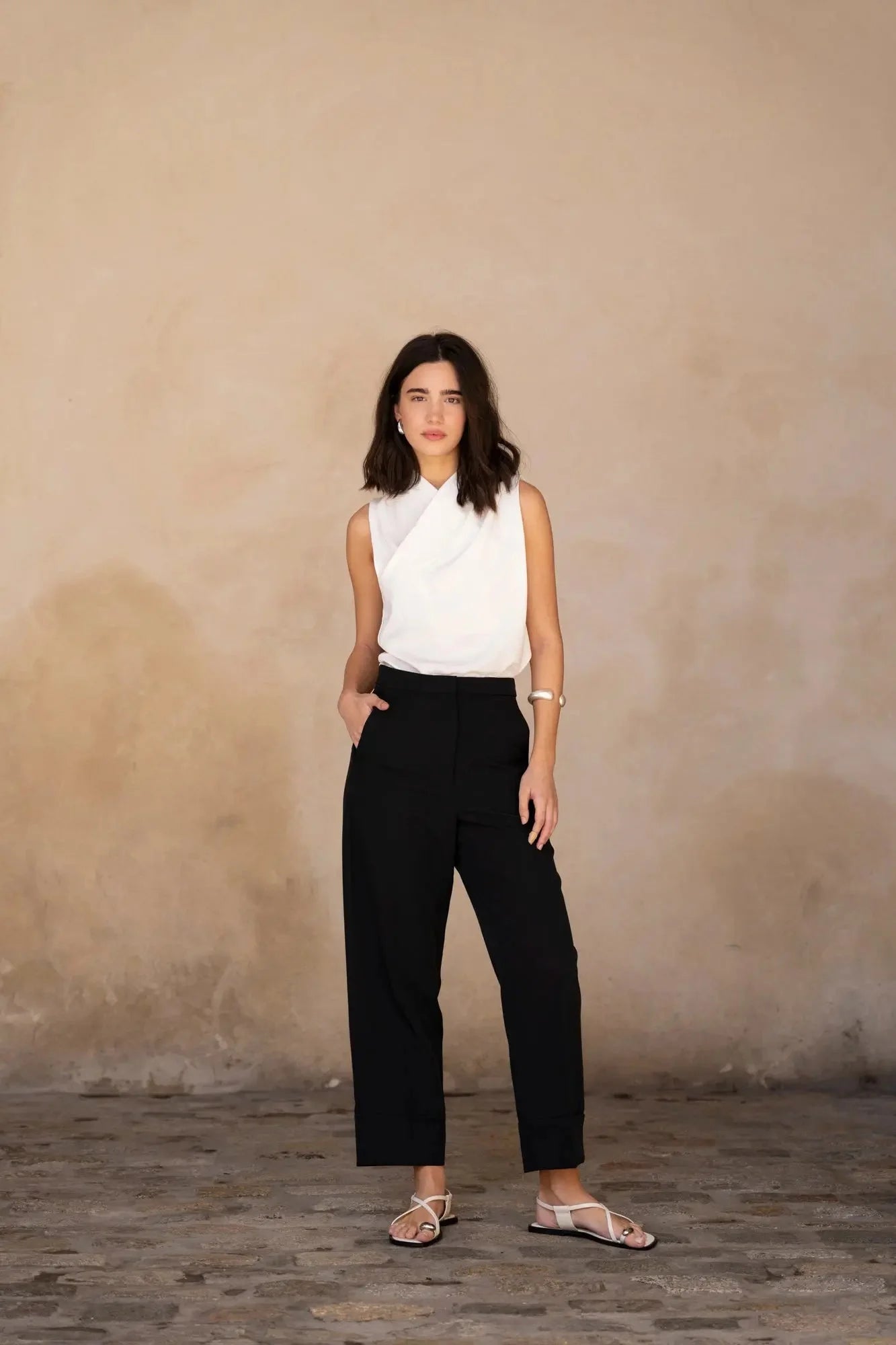 Femme en Top Croisé Devant Blanc Chic avec un pantalon noir, se tenant debout dans une pose détendue.