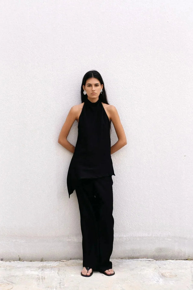 Portrait d'une femme en haut halter noir et pantalon assorti, soulignant le style minimaliste et moderne de ce haut long femme, parfait pour une sortie élégante.