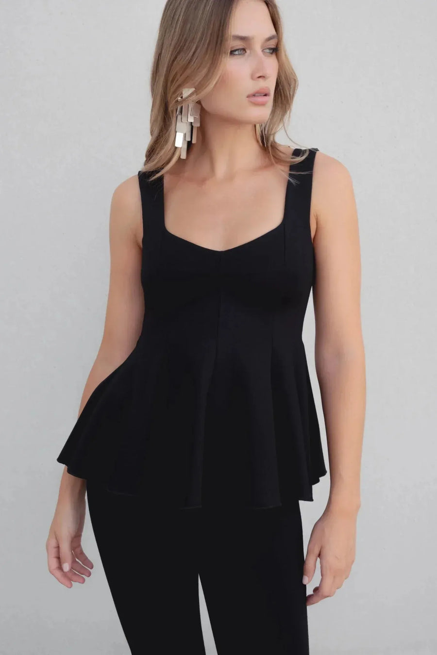 Modèle portant un top peplum femme noir élastique à encolure ronde, look chic et flatteur pour chaque occasion.