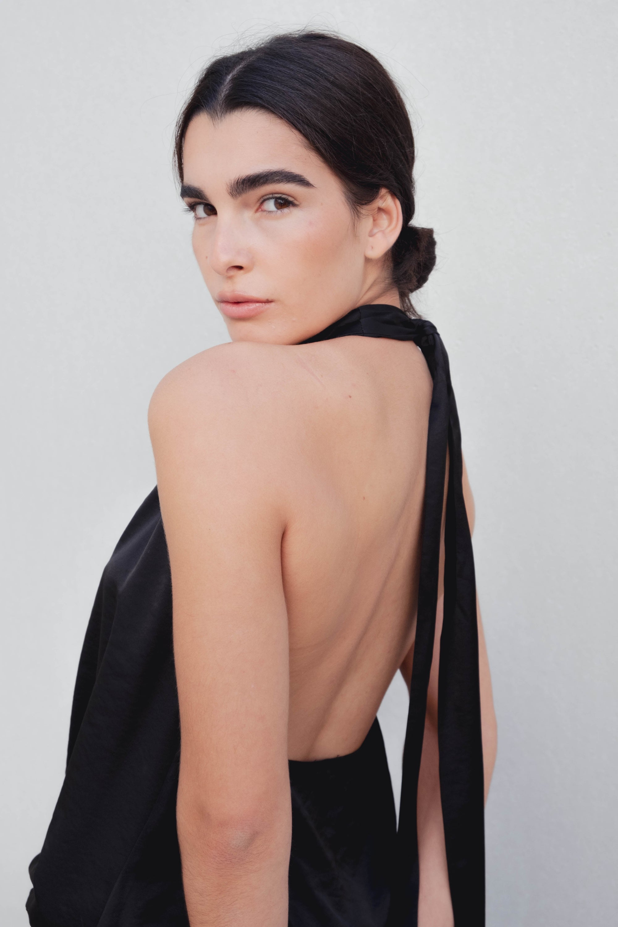 Femme montrant le top dos nu élégant – Col halter – Noir – Satin, accentuant la beauté du dos nu et le drapé.