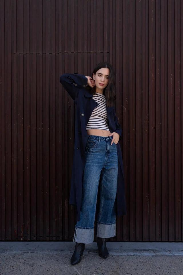 Modèle féminine portant un trench coat femme ample long ceinturé, associé à un haut rayé et un pantalon en denim.