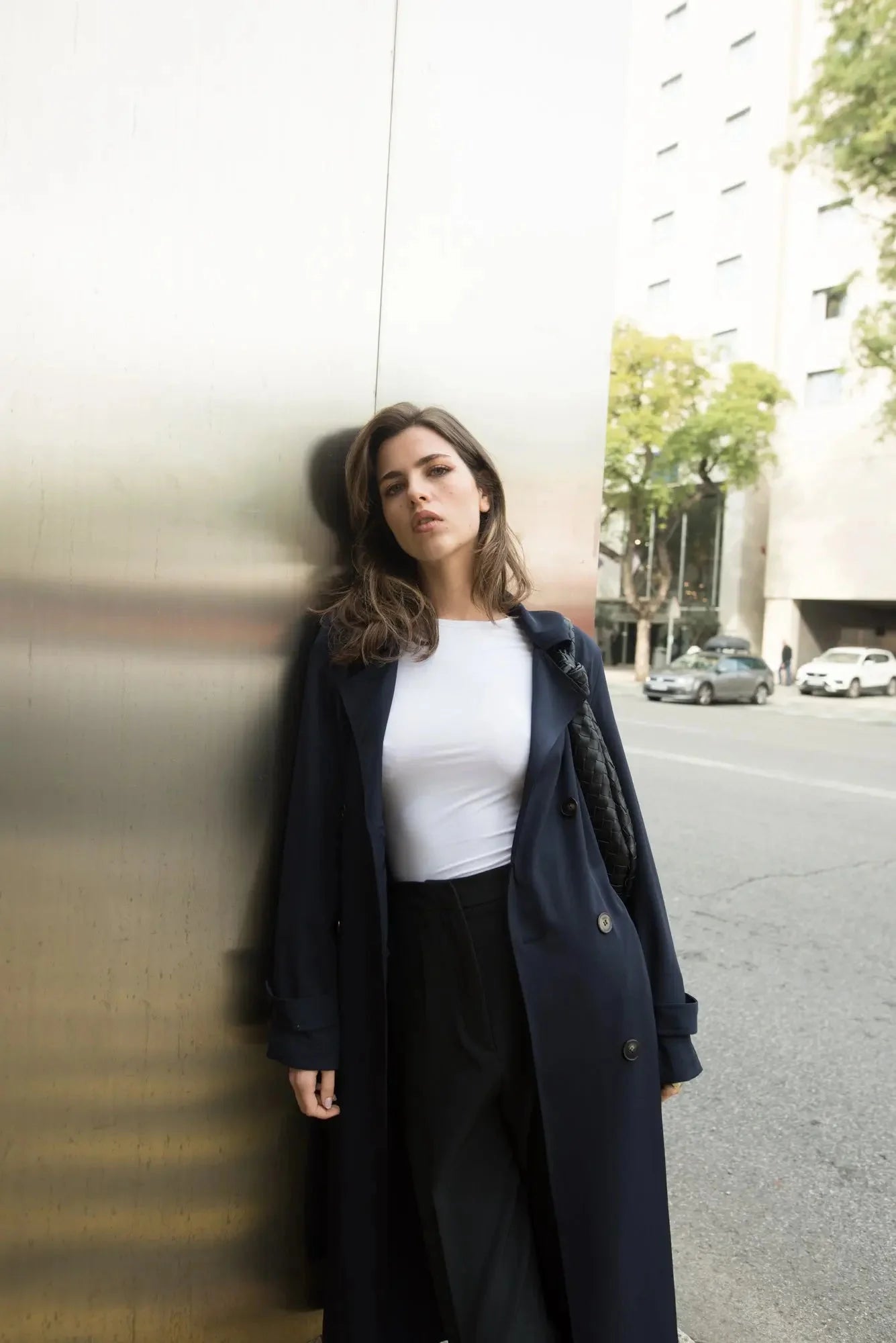 Femme portant un trench-coat ample navy avec ceinture, top blanc et pantalon noir
