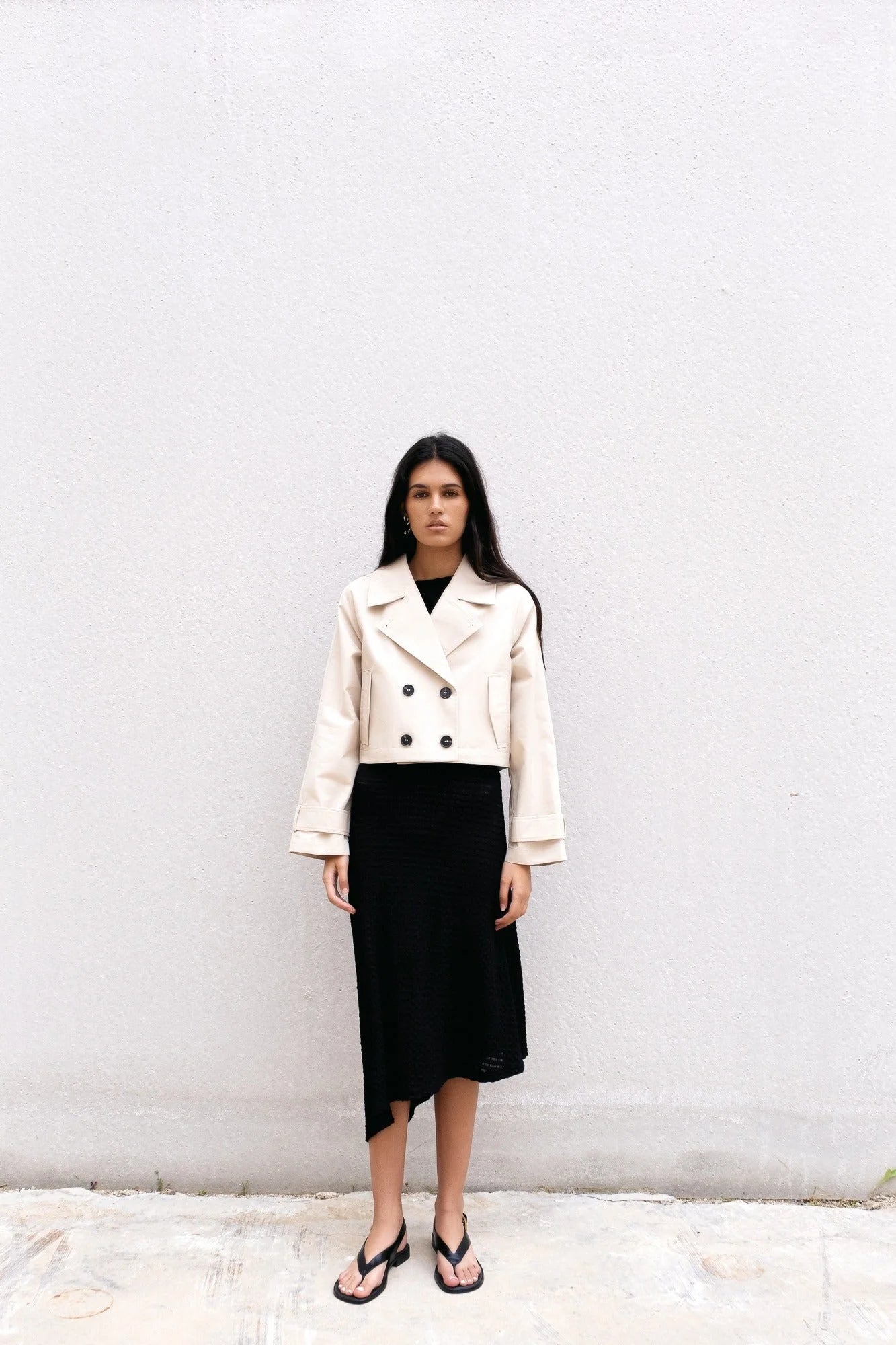Femme portant un trench coat court beige à double boutonnage et une robe noire midi