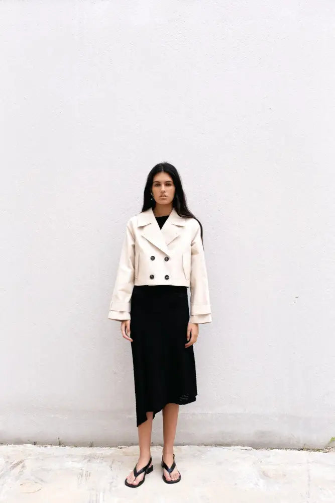 Femme portant un trench coat court beige à double boutonnage et une robe noire midi