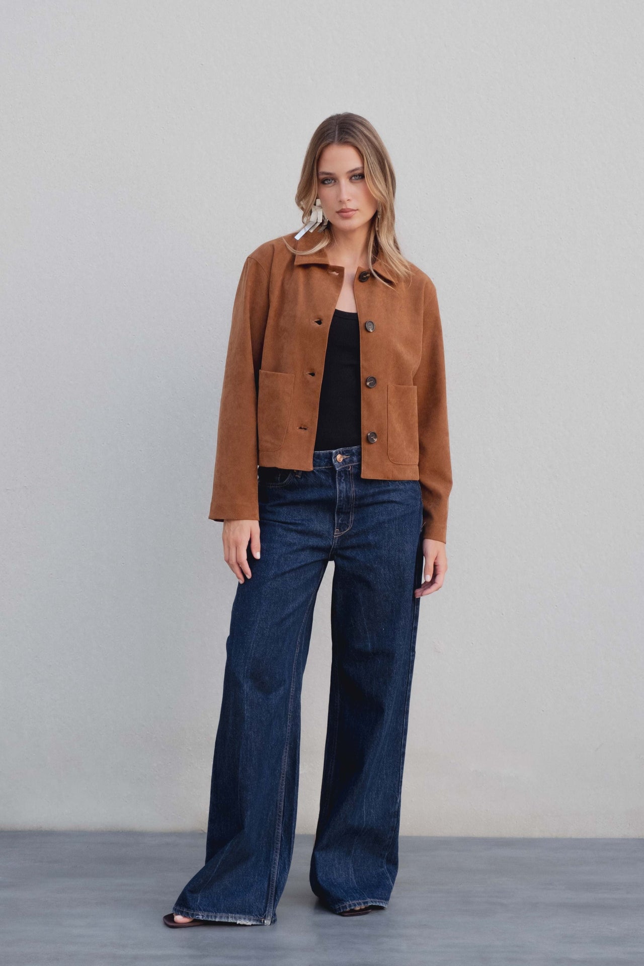 Femme posant avec une veste courte élégante coupe droite marron effet suède, associée à un pantalon en denim, parfaite pour un style urbain. Veste daim femme.